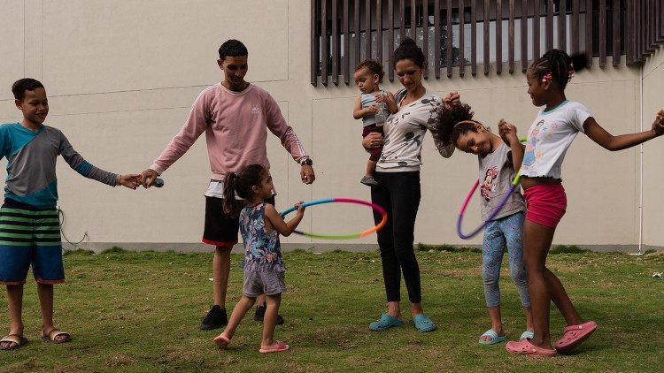 Enzor Figuera, imigrante venezuelano, brinca com os filhos enquanto espera receber formação e achar um emprego estável. (@Margherita Mirabella/Archivio GSF)