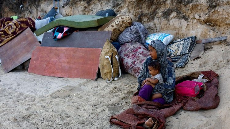 Uma mulher palestina com bebê se refugia na praia de Gaza.