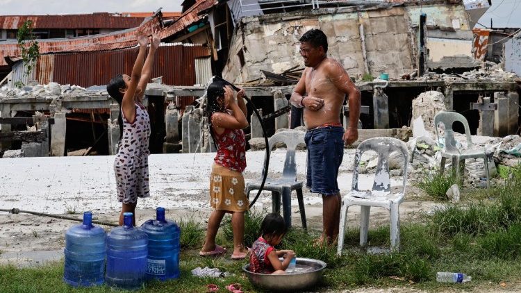 Família toma banho com mangueira, em frente à casas destruídas por terremoto em Bogo City.
